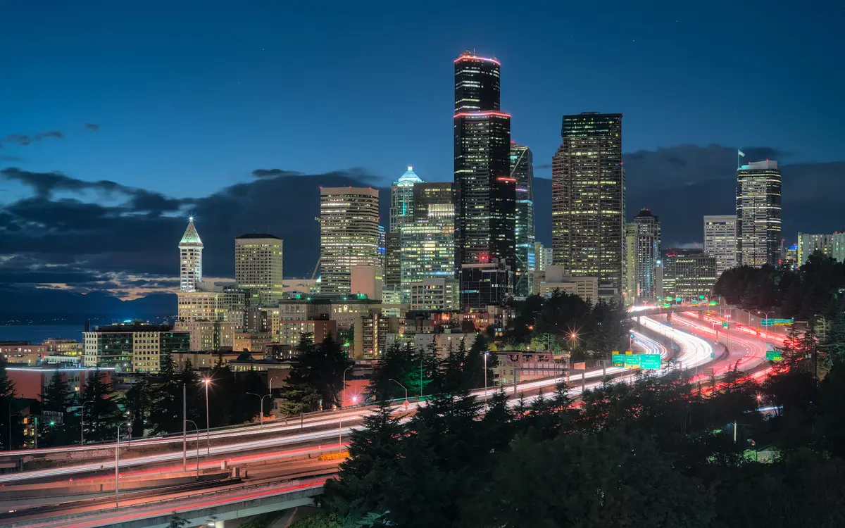 Web design in Seattle: The Seattle skyline at dusk as viewed from the Jose Rizal Bridge. In the foreground is the Interstate 5 in Washington.